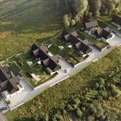 Nowoczesne domy z ciemnymi dachami i ogrodami, otoczone zielenią. Widok z lotu ptaka, jakby z **timelapse** pokazujący rozwój osiedla.