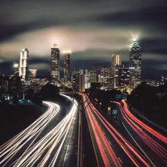 Nocne miasto w technice time lapse. Smugi świateł samochodów na autostradzie przed oświetlonymi wieżowcami.