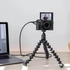 Ustawienie do streamingu: laptop z widokiem na uśmiechniętego mężczyznę, kamera Canon G7X na statywie Joby, wykorzystująca funkcje EOS Utility.