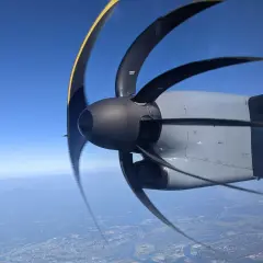 Wirujący śmigłowiec samolotu z efektem rolling shutter nad miastem i górami w oddali.