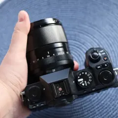 Dłoń trzyma aparat Fujifilm X-S20 z obiektywem. Widoczne pokrętła trybów i przyciski.