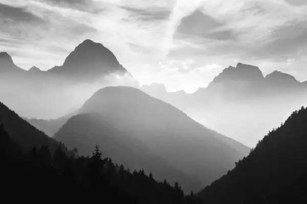 Mgliste pasmo górskie w ujęciu monochromatycznym. W oddali widać ostre szczyty, bliżej łagodne, zalesione wzgórza.