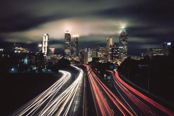 Nocne miasto w technice time lapse. Smugi świateł samochodów na autostradzie przed oświetlonymi wieżowcami.